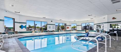 A swimming pool with white railings, lounge chairs, and a view of the outdoors.