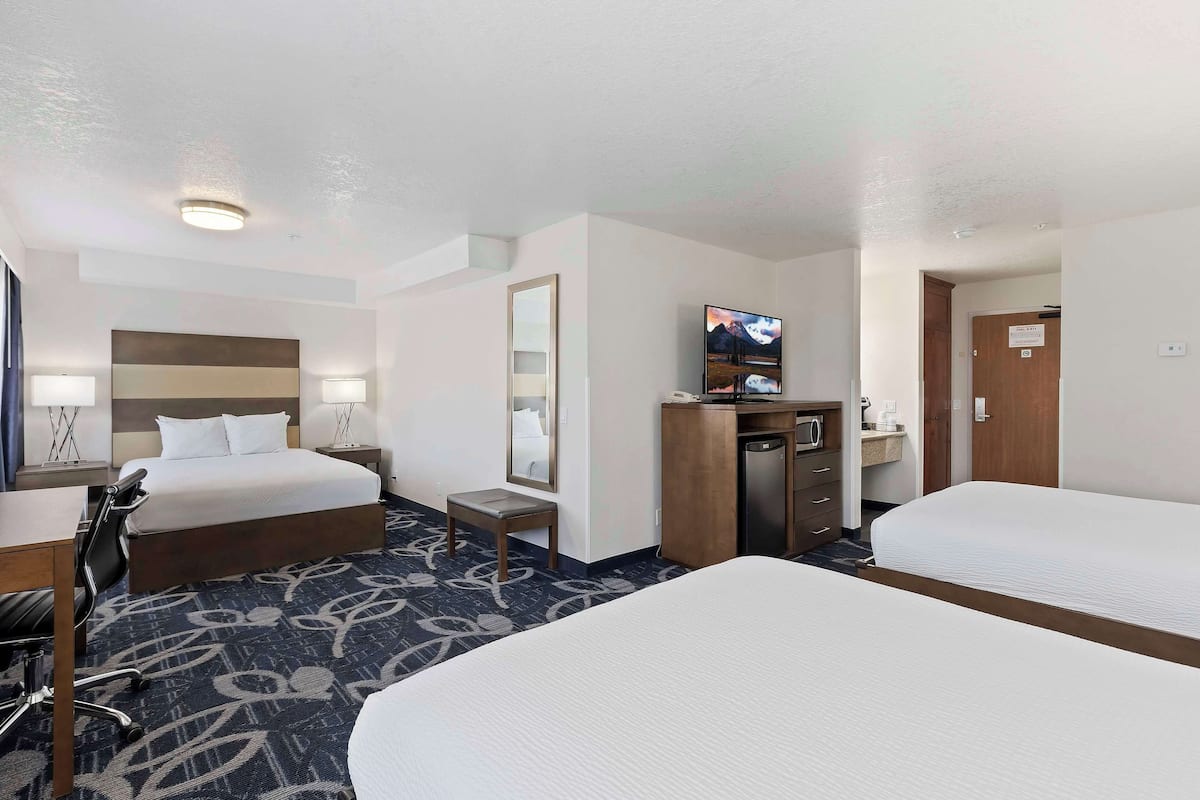 A hotel room with two beds, a desk, a chair, a TV, and a bathroom.