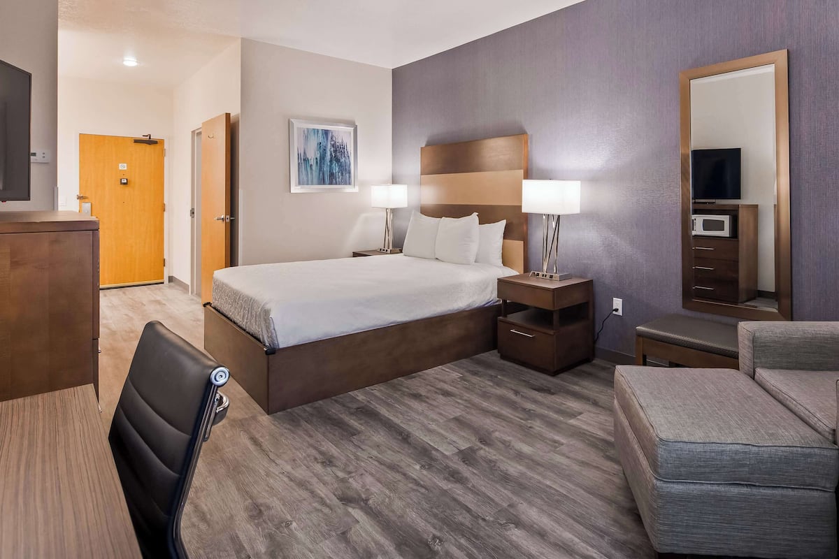 A hotel room with a bed, bedside tables, a chair, a desk, and a large mirror.