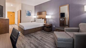 A hotel room with a bed, bedside tables, a chair, a desk, and a large mirror.