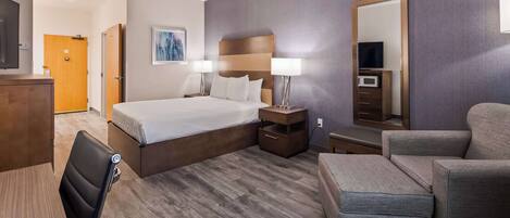 A hotel room with a bed, bedside tables, a chair, a desk, and a large mirror.