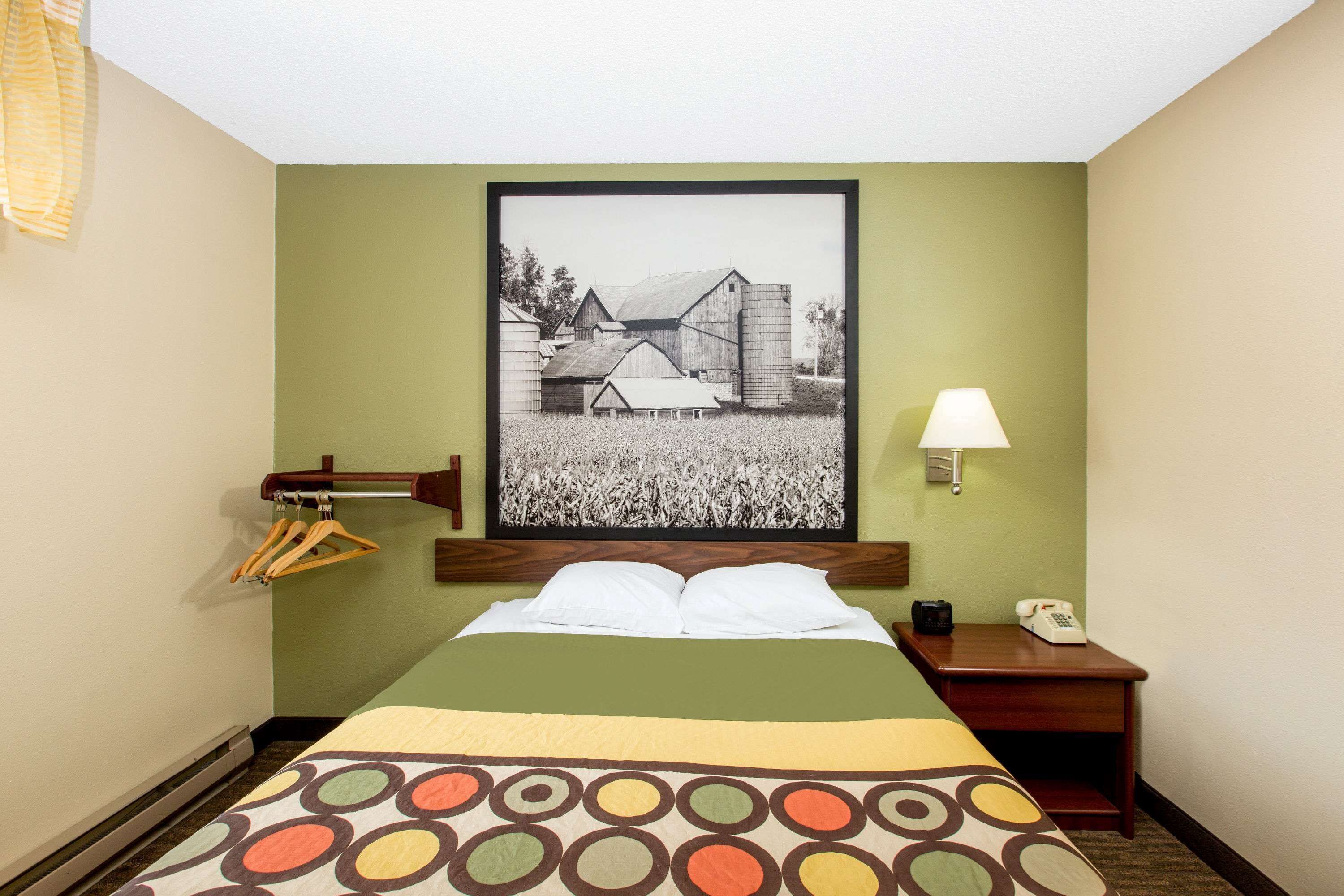 A hotel room with a bed, a nightstand, a lamp, a telephone, and a framed picture on the wall.