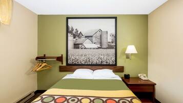 A hotel room with a bed, a nightstand, a lamp, a telephone, and a framed picture on the wall.