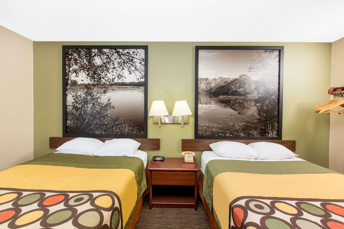 Une chambre d’hôtel avec deux lits, des murs verts et deux grands tableaux représentant des paysages.