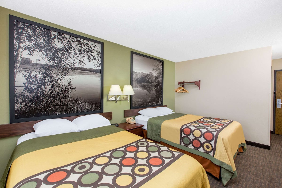 Une chambre d’hôtel avec deux lits, chacun recouvert d’une couvre-lit à motifs, une table de chevet avec une lampe et une étagère fixée au mur.