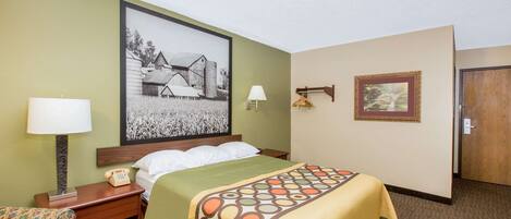 A hotel room with a bed, a desk with a lamp, a chair, and a picture on the wall.