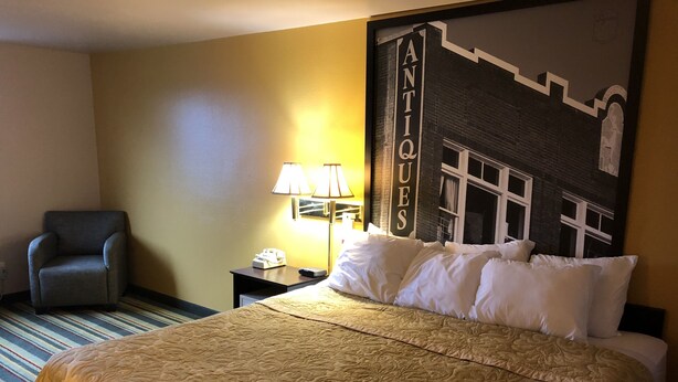 A hotel room with a large bed, a chair, a nightstand with a lamp, and a wall with a 'ANTIQUE' sign. - Super 8 by Wyndham Coeur d'Alene (Coeur d'Alene)