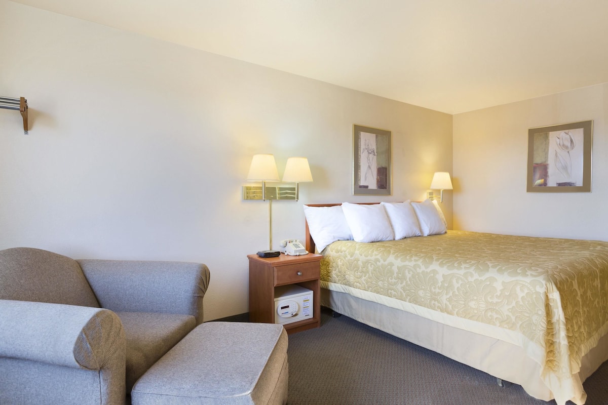 A hotel room with a bed, a sofa, a nightstand with a lamp, and a small table.