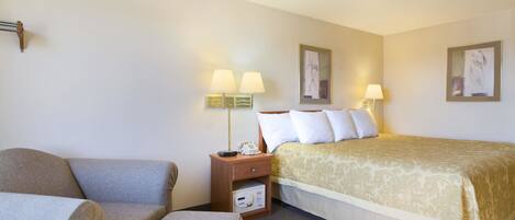 Quarto de hotel com cama, sofá, mesa de cabeceira com abajur e uma pequena mesa.
