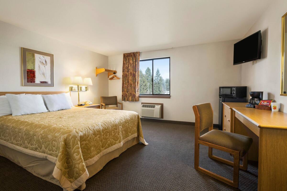 A hotel room with a large bed, a desk with a chair, a television, and a window with curtains.