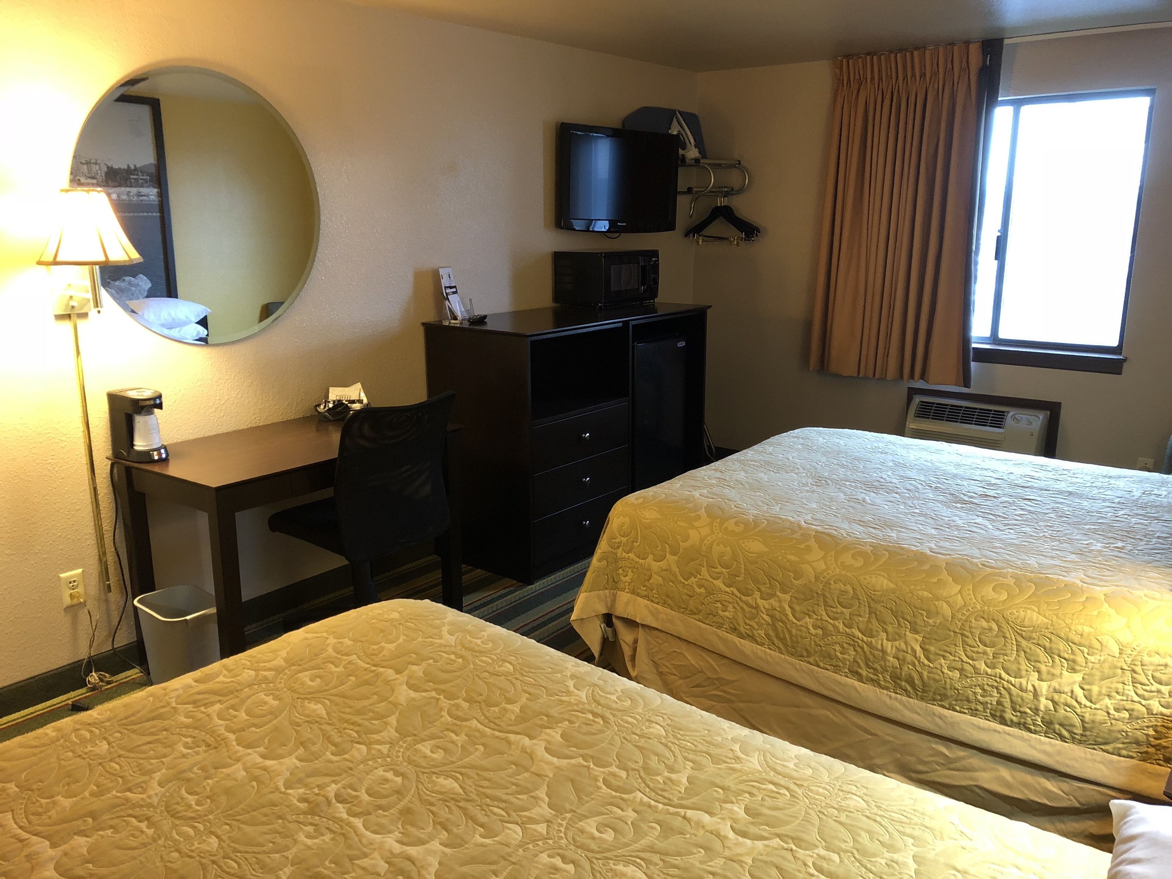 Habitación de hotel con dos camas, un escritorio, una silla, un televisor y una ventana con cortinas.