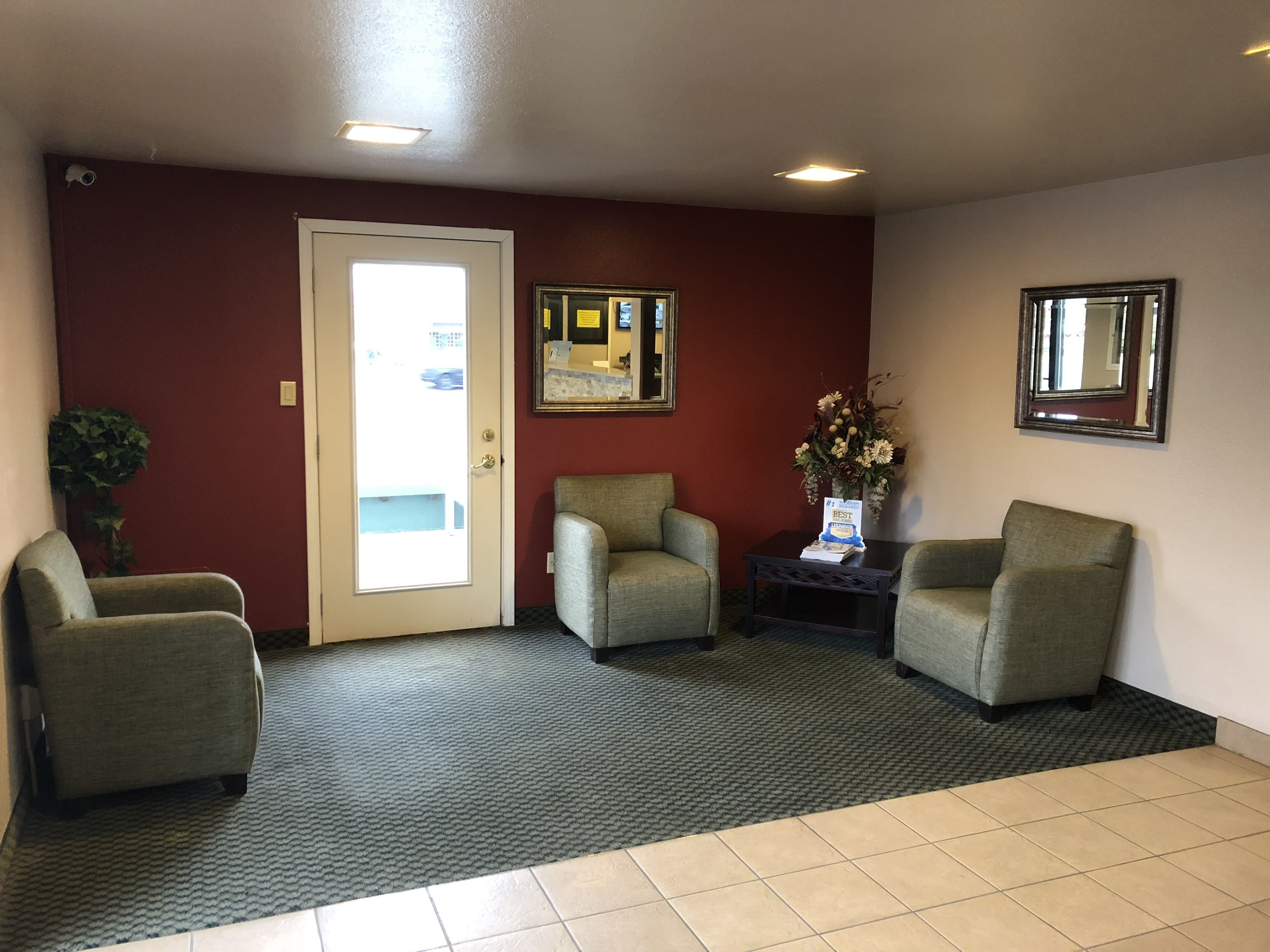 A waiting area with three armchairs, a small table with a vase of flowers, and a door leading outside.