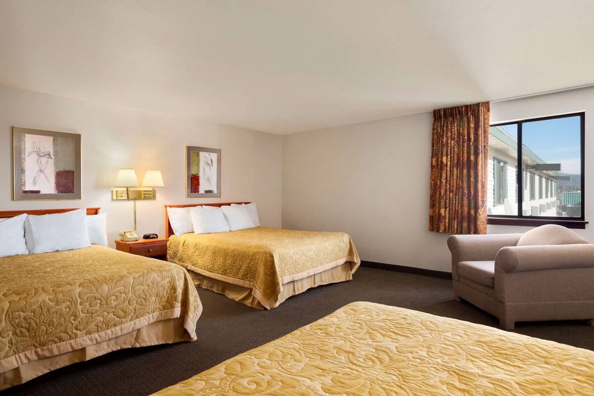 A hotel room with two beds, a chair, a nightstand with a lamp, and a window with a view.