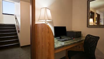 Een hotelkamer met een houten bureau, een computer, een stoel, een lamp en een trap.