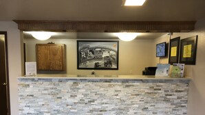 A reception desk with a stone mosaic top, wooden cabinets, framed pictures, and informational signs. - Super 8 by Wyndham Coeur d'Alene (Coeur d'Alene)