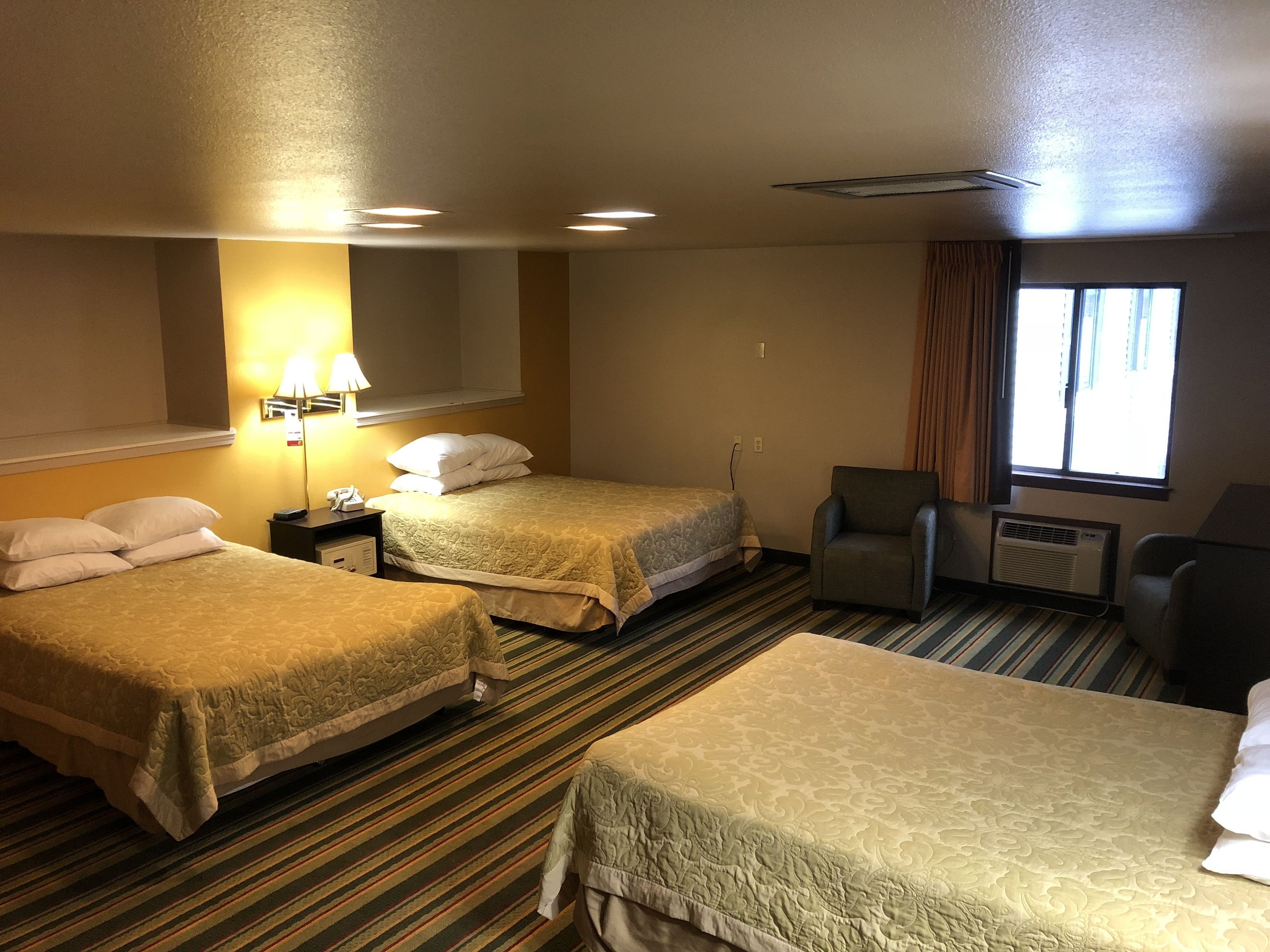 A hotel room with two beds, a desk with a lamp, a chair, and a window with curtains.