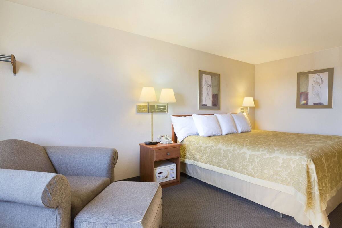 A hotel room with a bed, a chair, a nightstand with a phone, and two wall-mounted lamps.