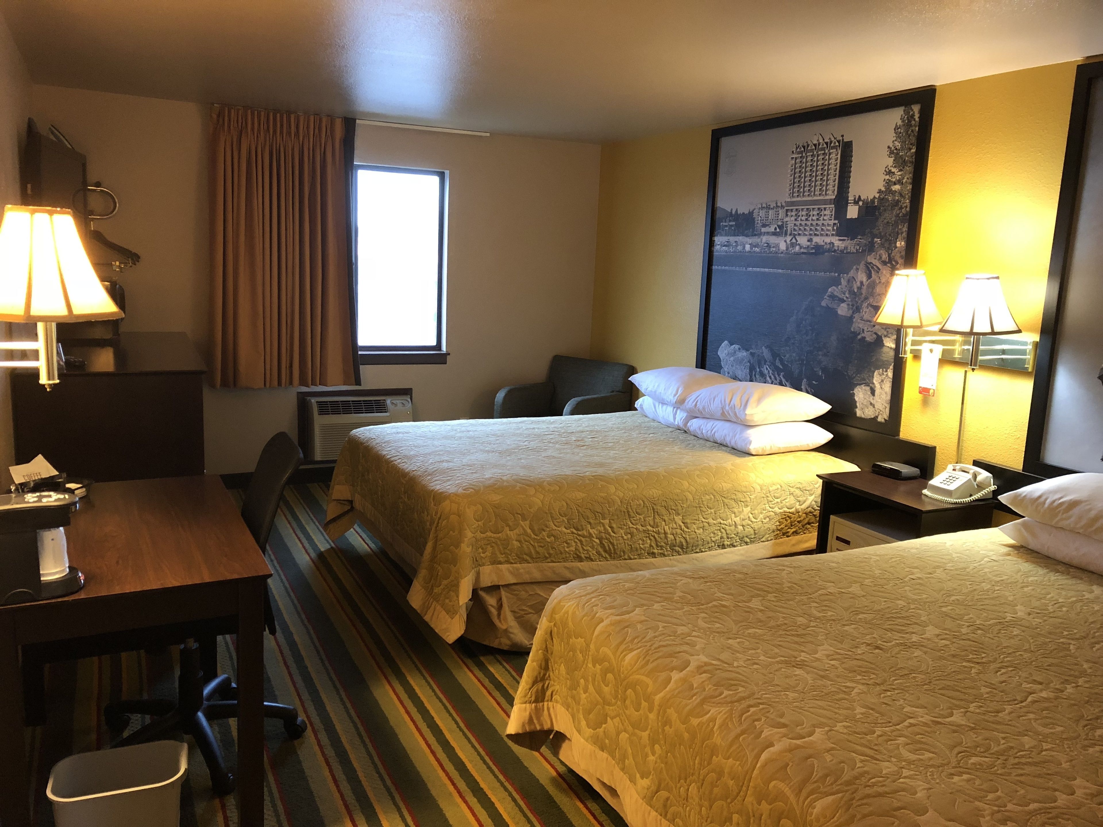 Een hotelkamer met twee bedden, een bureau, een stoel, een telefoon en een raam met gordijnen.