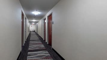 Un couloir d’hôtel avec des revêtements de sol en moquette, des portes de chaque côté et un éclairage au plafond.