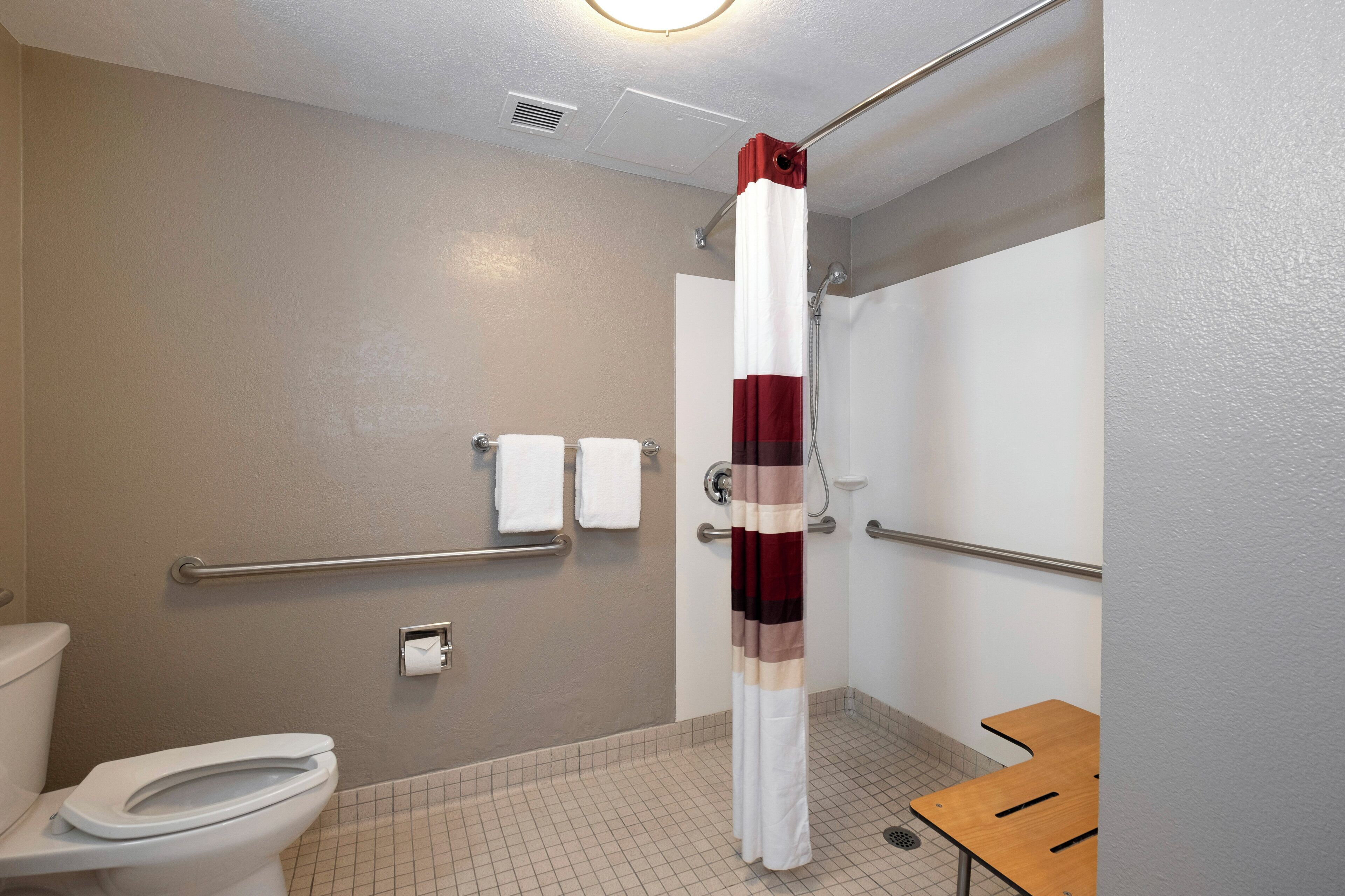 A bathroom with a toilet, a shower with a red and white striped curtain, and a grab bar.