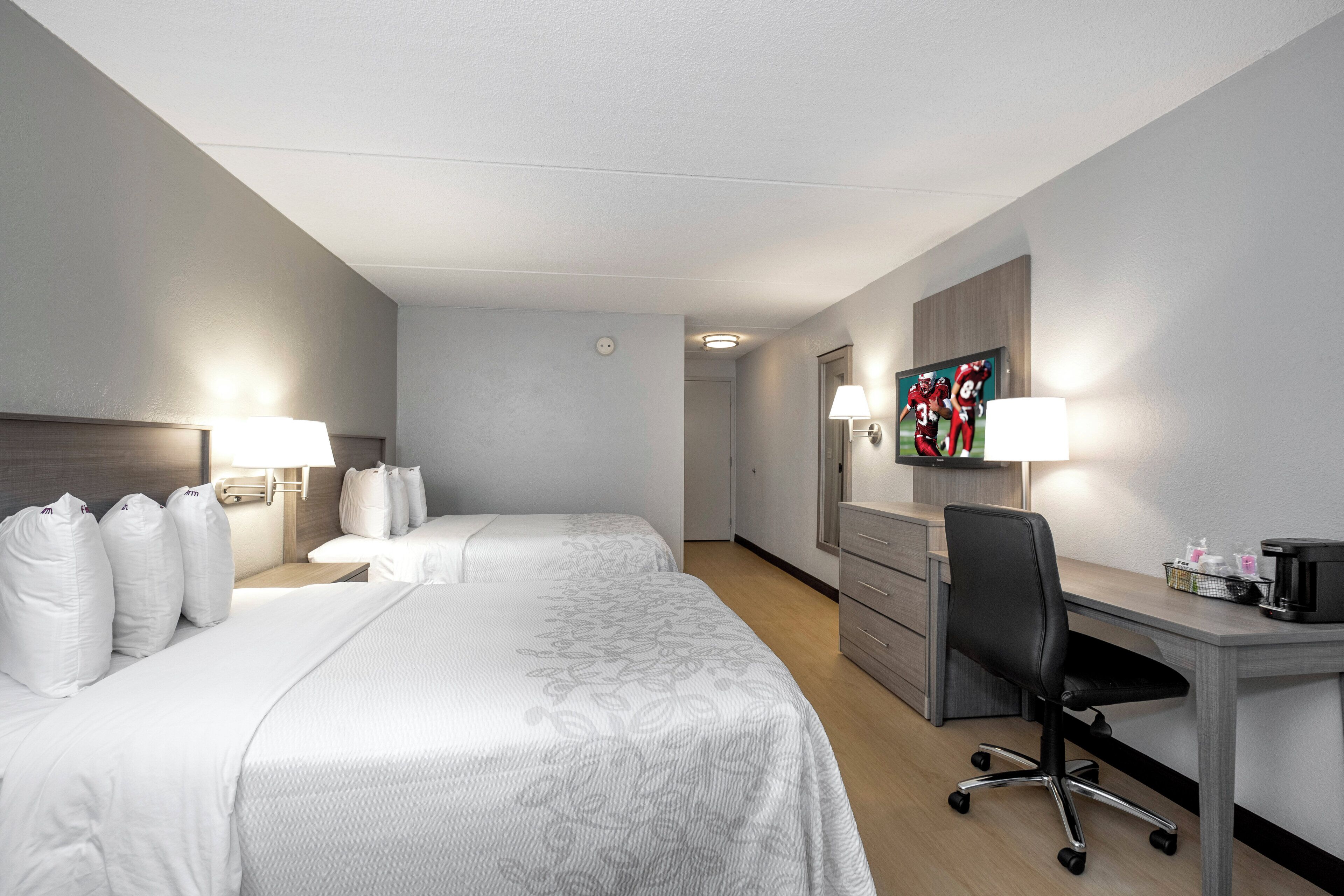 A hotel room with two beds, a desk, a chair, a television, and a coffee maker.