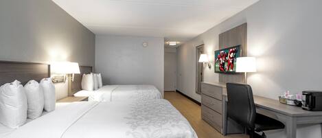 A hotel room with two beds, a desk, a chair, a television, and a coffee maker.