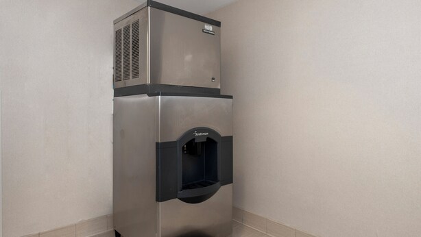A stainless steel commercial refrigerator with a water dispenser, located in a corner with tiled flooring. - Red Roof Inn PLUS+ Boston - Mansfield/ Foxboro (Mansfield)