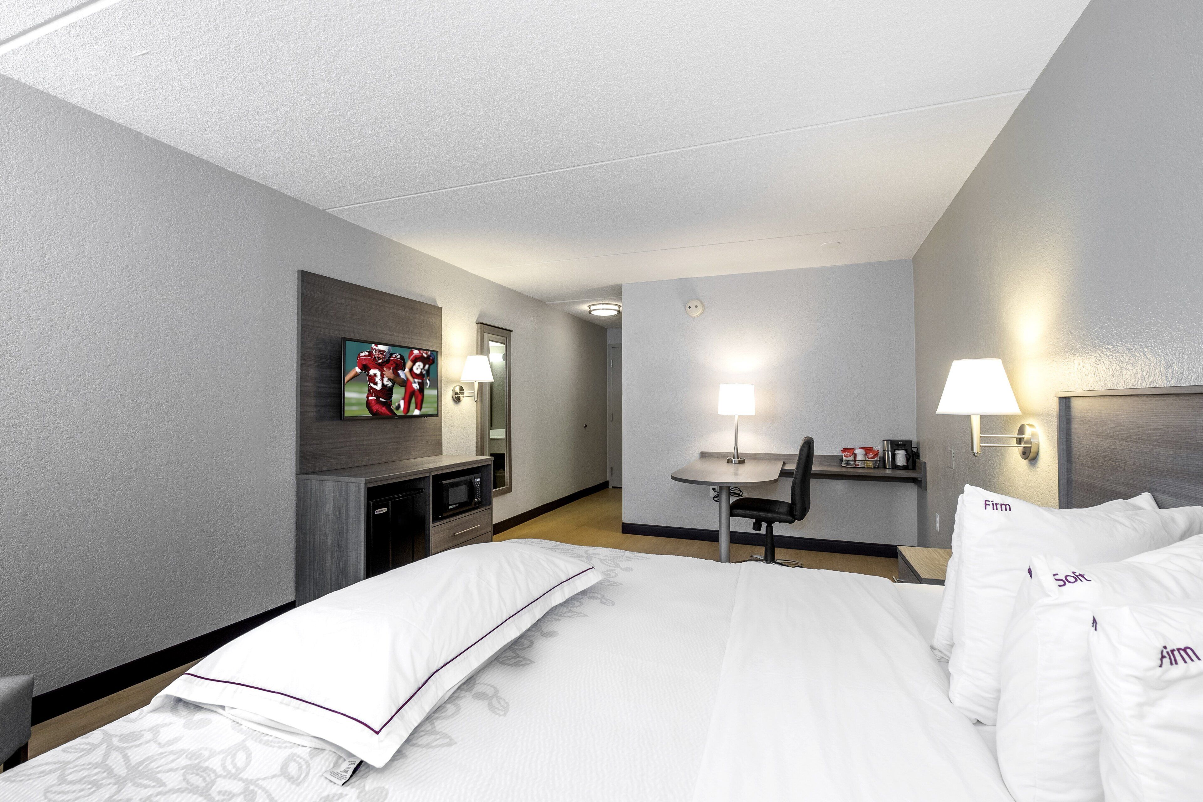 A hotel room with a bed, a desk, a chair, a television, and a microwave.