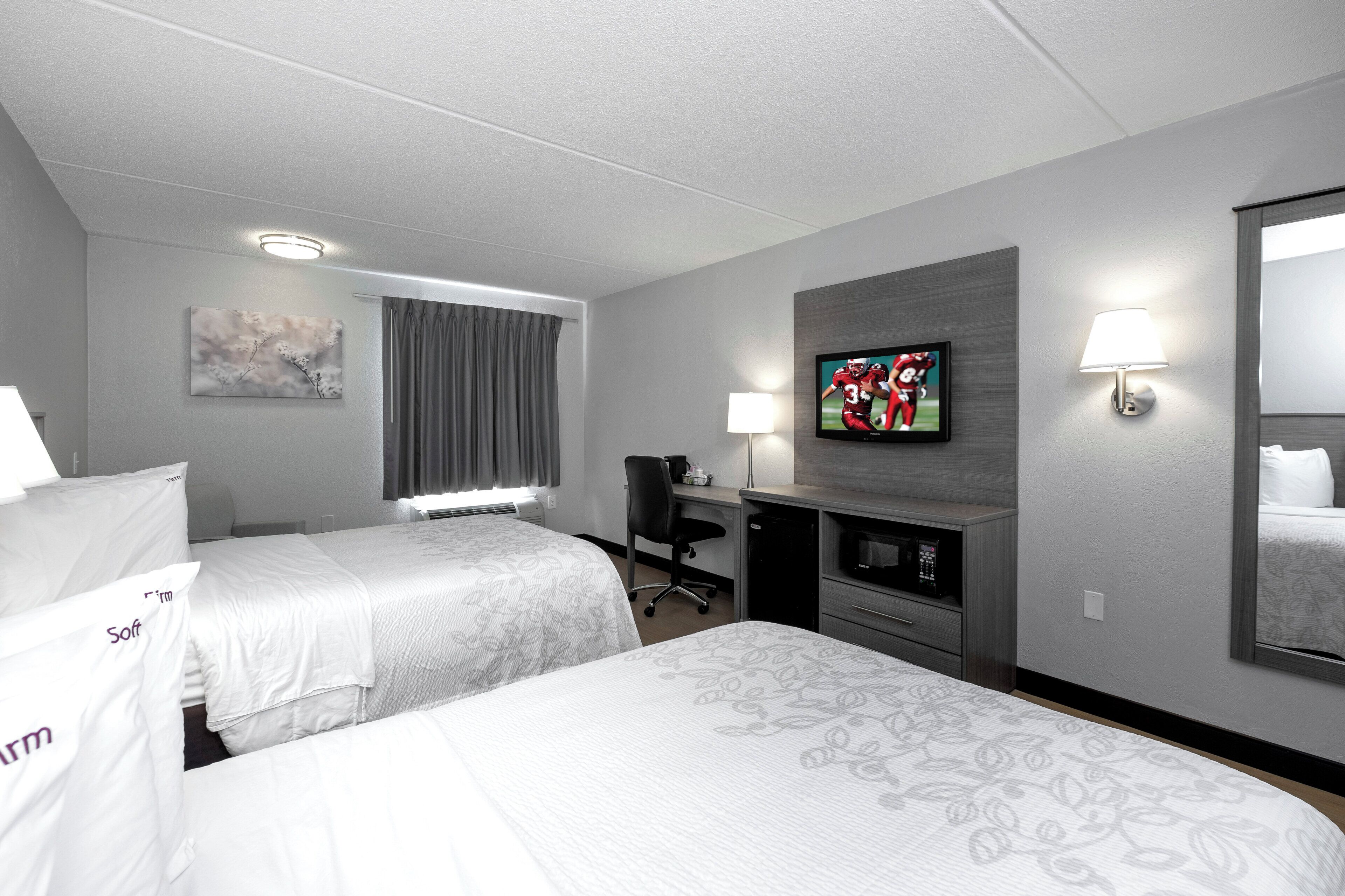 A hotel room with two beds, a desk, a television, and a window with curtains.