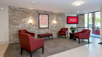 A hotel lobby with a stone wall, red chairs, a bench, a TV screen advertising free Wi-Fi, and a framed sign for Red Roof Plus.