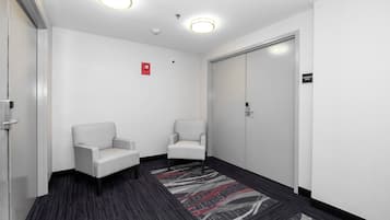 A hallway with two white armchairs, a carpeted floor, a door labeled 'Conference Room', and ceiling lights.