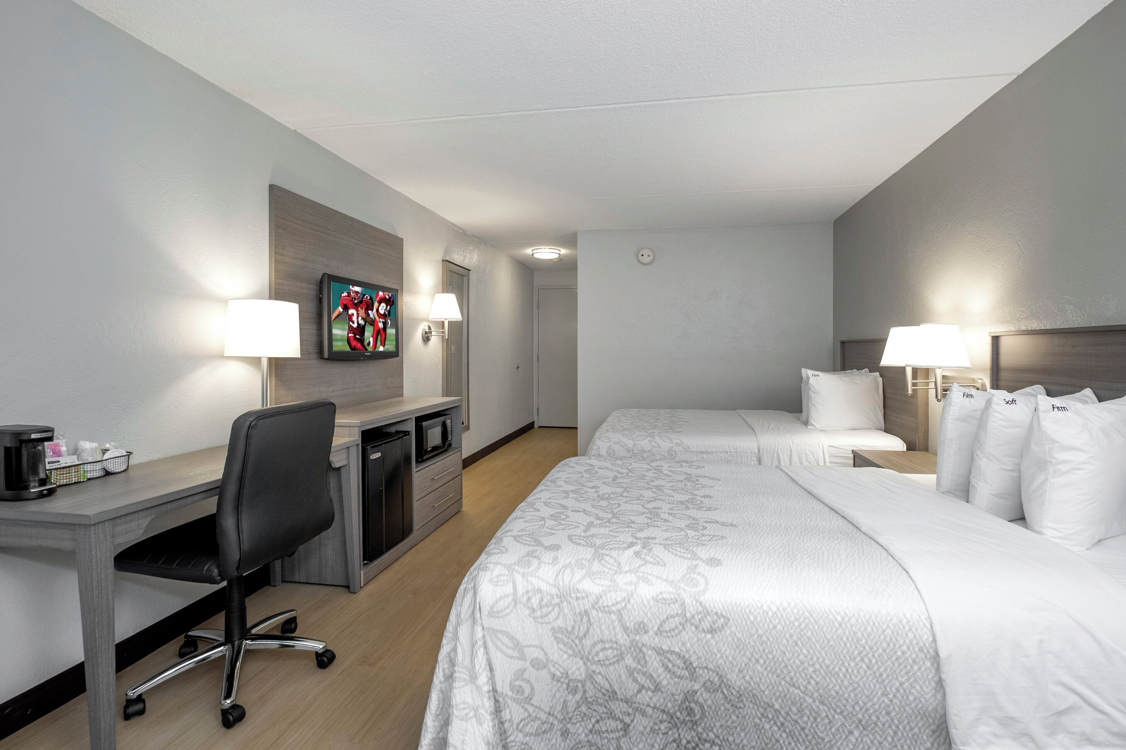 Una habitación de hotel con cama, escritorio con silla, televisor y dos lámparas de noche.