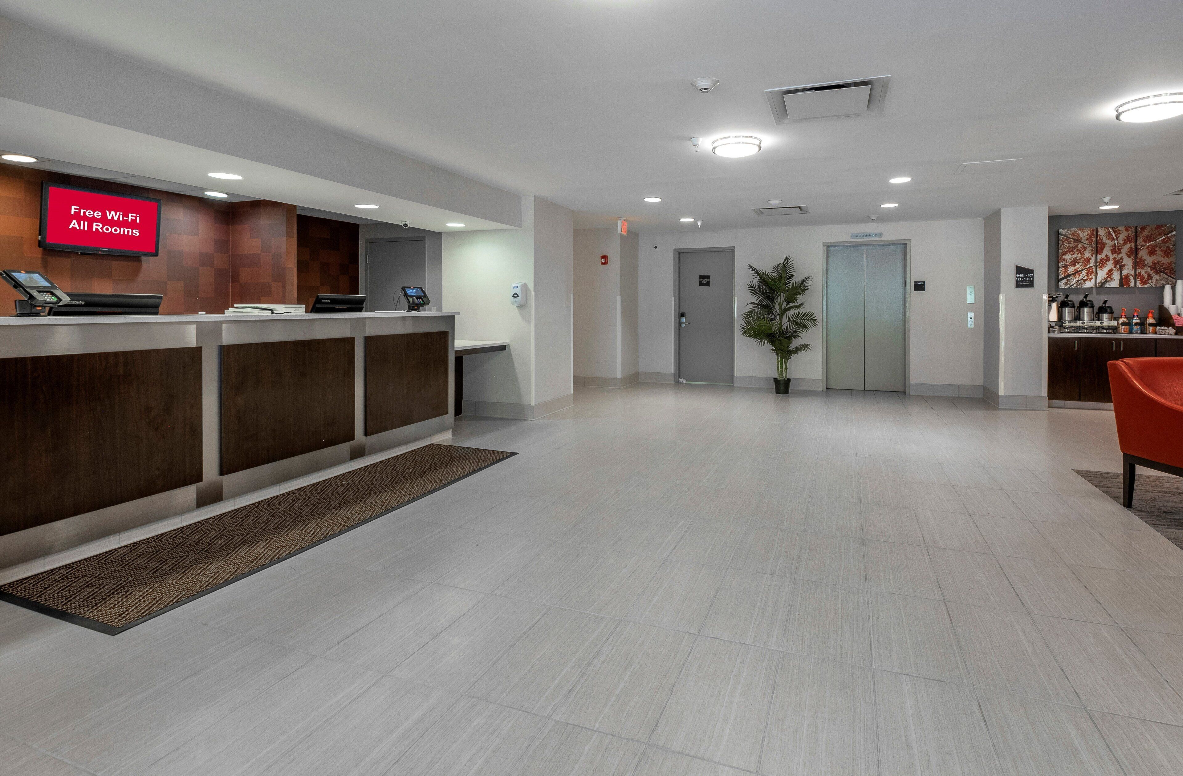 A hotel reception area with a digital display indicating free Wi-Fi availability, a reception desk, a potted plant, and an elevator.