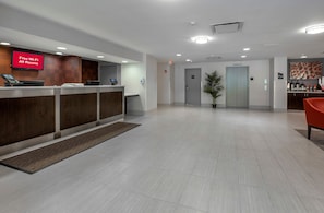 A hotel reception area with a digital display indicating free Wi-Fi availability, a reception desk, a potted plant, and an elevator. - Red Roof Inn PLUS+ Boston - Mansfield/ Foxboro (Mansfield)