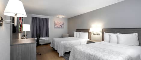 A hotel room with two beds, a desk, a chair, a window with curtains, and a painting on the wall.