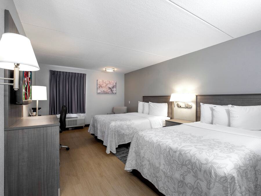 A hotel room with two beds, a desk, a chair, a window with curtains, and a painting on the wall.