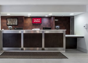 A reception desk with a digital display, a 'Free Wi-Fi All Rooms' sign, and a security camera. - Red Roof Inn PLUS+ Boston - Mansfield/ Foxboro (Mansfield)