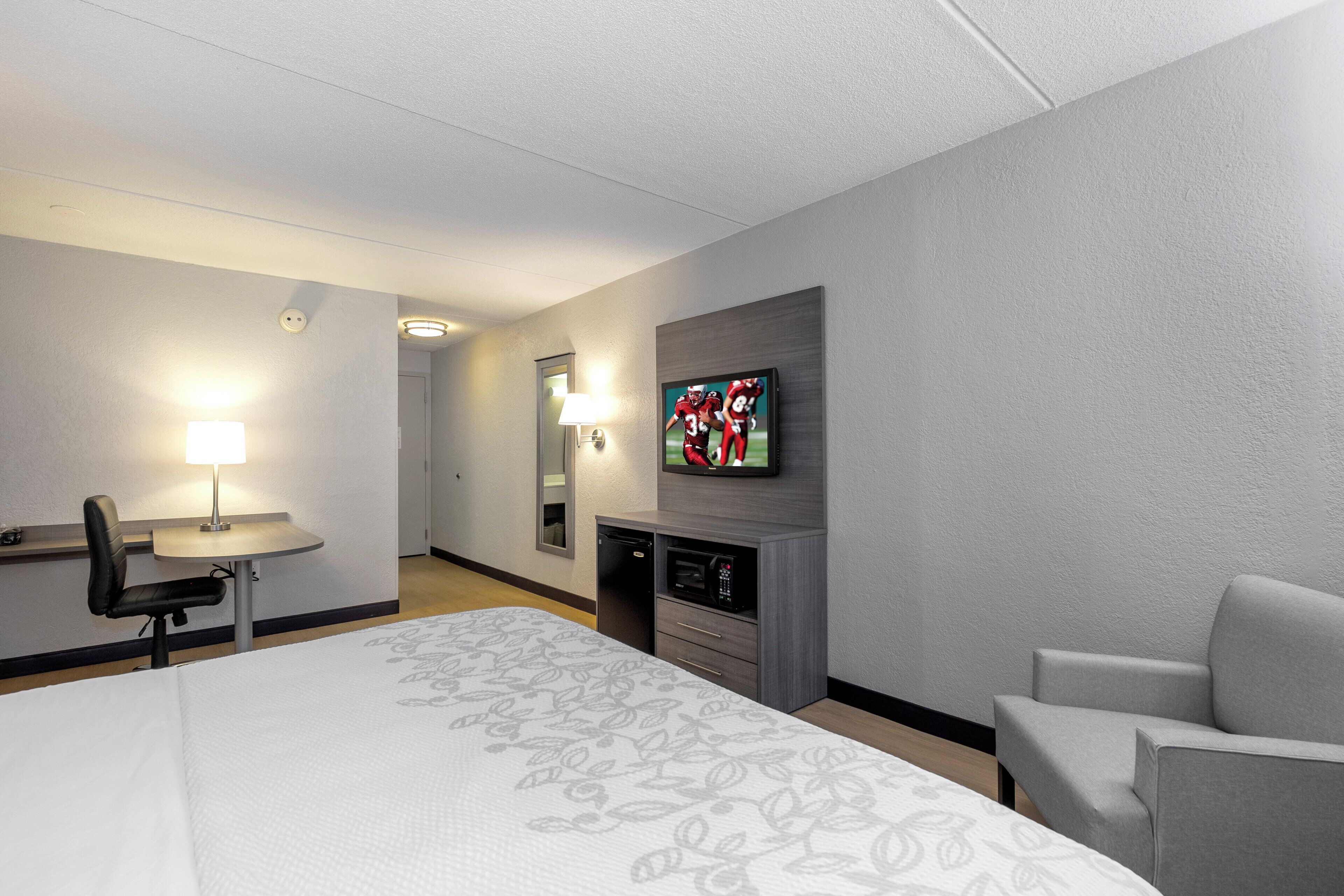 A hotel room with a bed, a desk, a chair, a television, and a microwave.