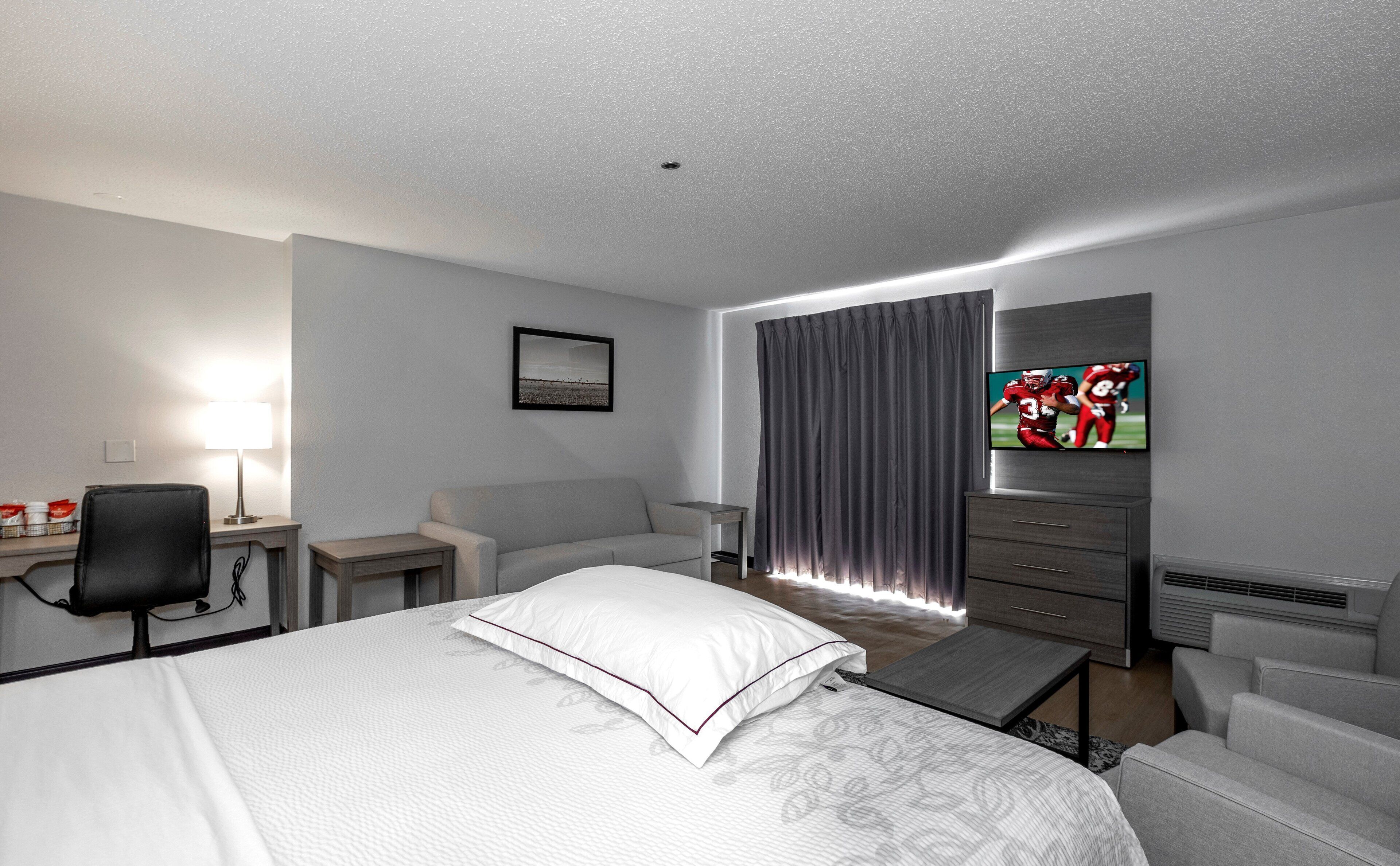 A hotel room with a bed, a desk, a chair, a television, and a window with curtains.