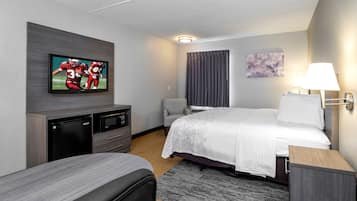 Una habitación de hotel con cama, televisión montada en la pared, escritorio, silla y lámpara.