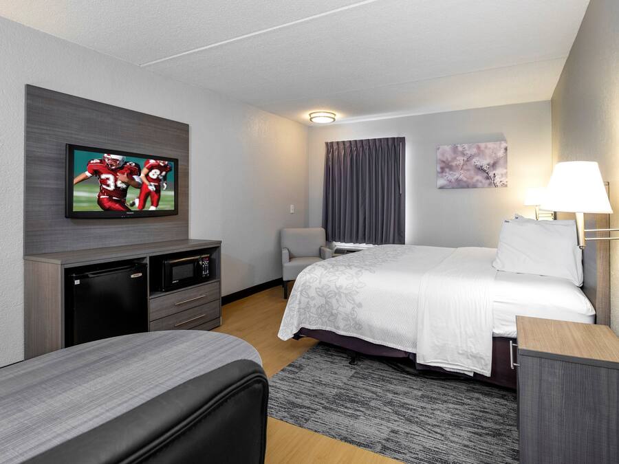 Una habitación de hotel con cama, televisión montada en la pared, escritorio, silla y lámpara.