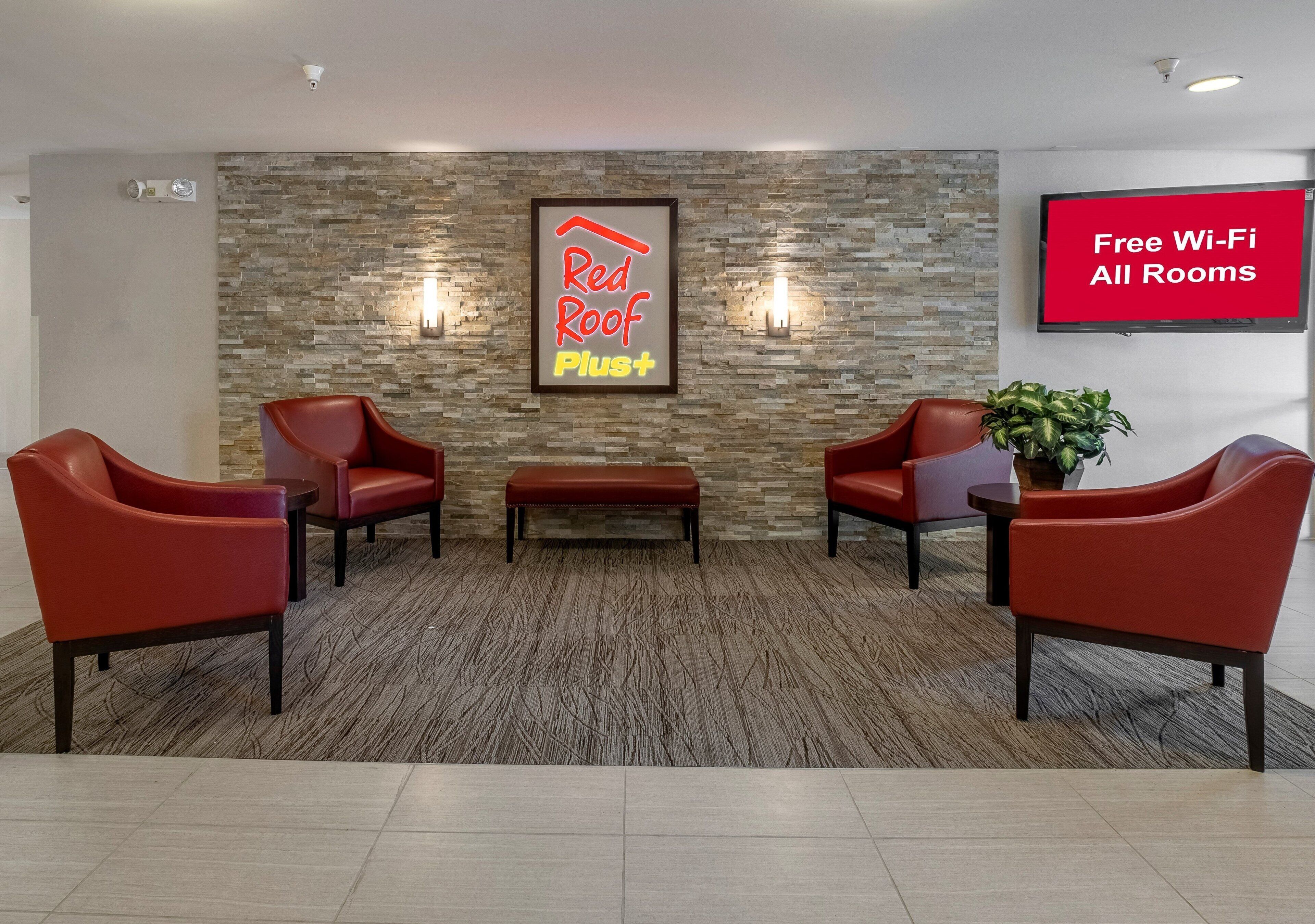 A lobby with a stone wall, two red chairs, a bench, a potted plant, and a TV screen advertising free Wi-Fi.