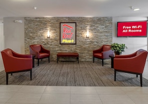 Un vestíbulo con pared de piedra, dos sillones rojos, un banco, una planta en maceta y una pantalla de televisión que anuncia Wi-Fi gratuito.