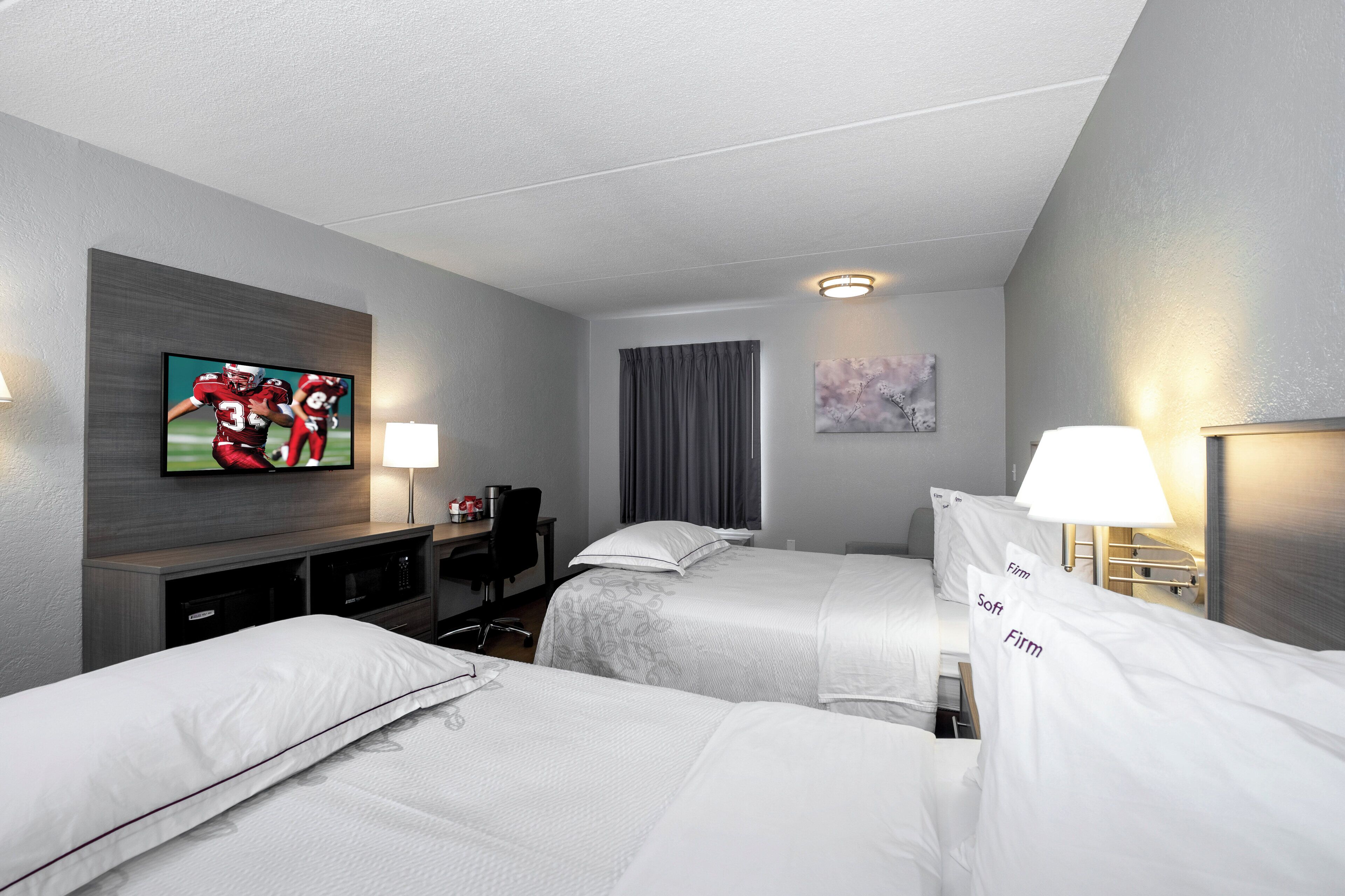 Une chambre d’hôtel avec deux lits, un bureau, une télévision et une fenêtre avec des rideaux.