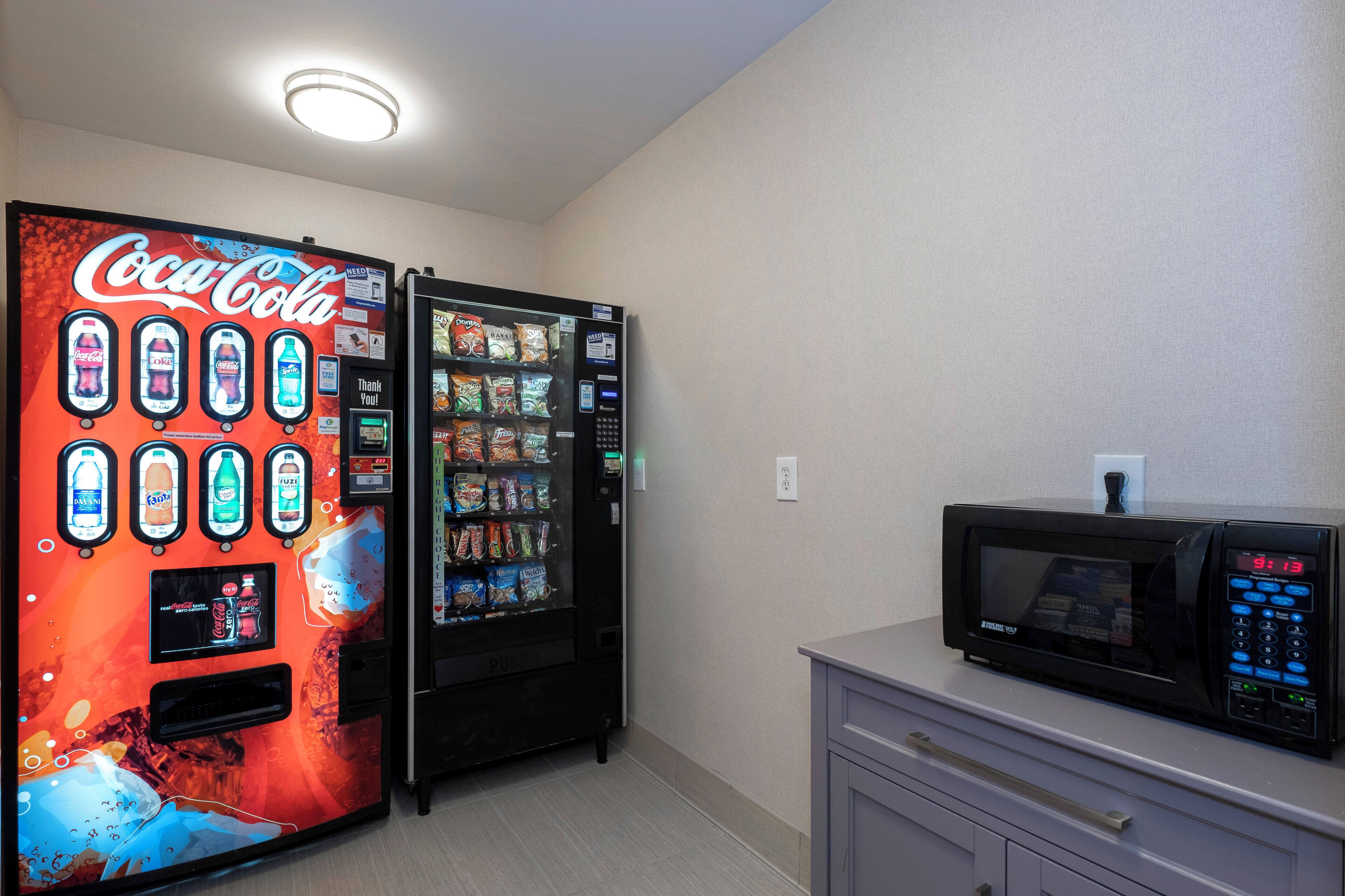 A vending machine area with a Coca-Cola machine and a microwave on a counter.