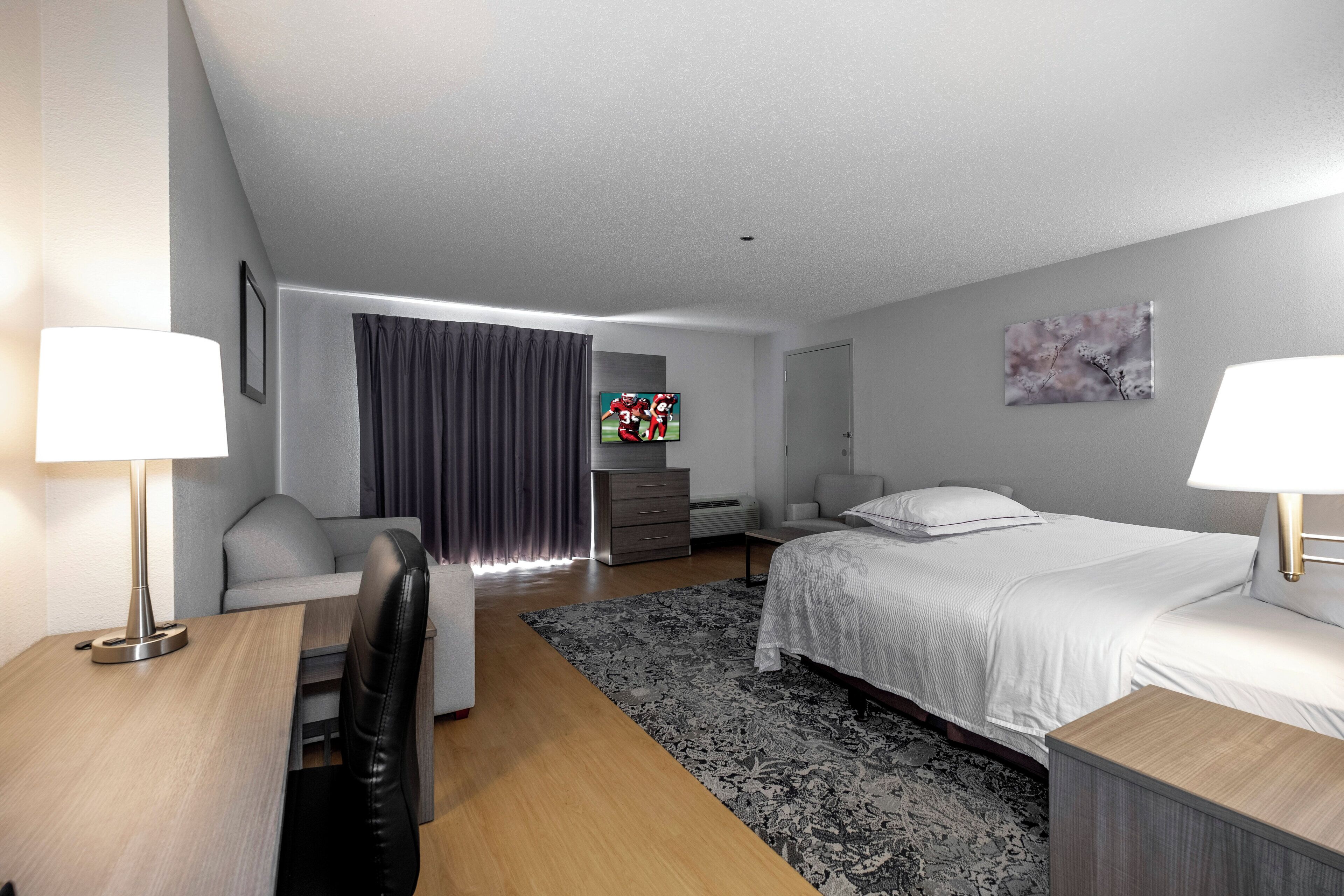 Una habitación de hotel moderna con cama, escritorio, sillón, sofá, televisor y un cuadro en la pared.