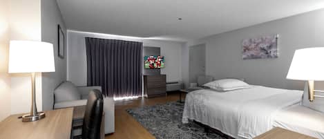 Una habitación de hotel moderna con cama, escritorio, sillón, sofá, televisor y un cuadro en la pared.