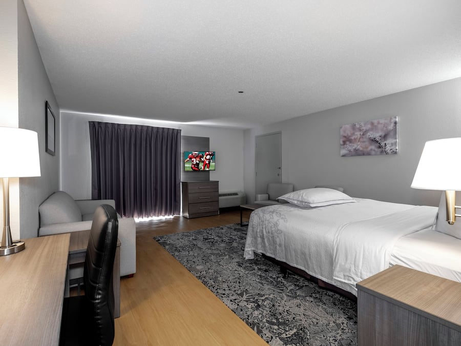 A modern hotel room with a bed, a desk, a chair, a sofa, a TV, and a painting on the wall.