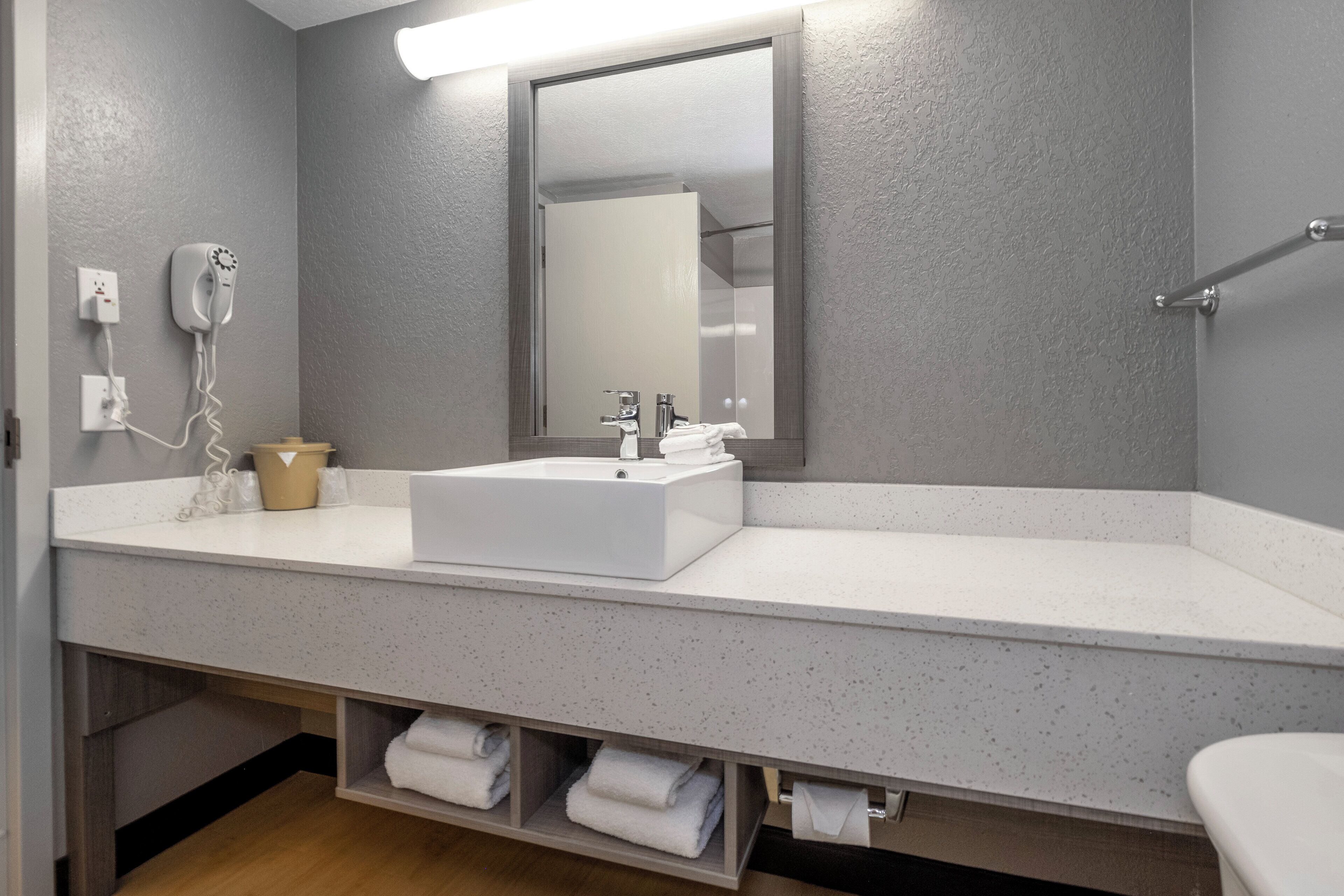 A modern bathroom with a white sink, a mirror above it, and a towel rack on the wall.
