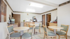 A dining area with round tables and chairs, a kitchen in the background, and a clock on the wall. - FairBridge Inn & Suites Moscow/Pullman (Moscow)